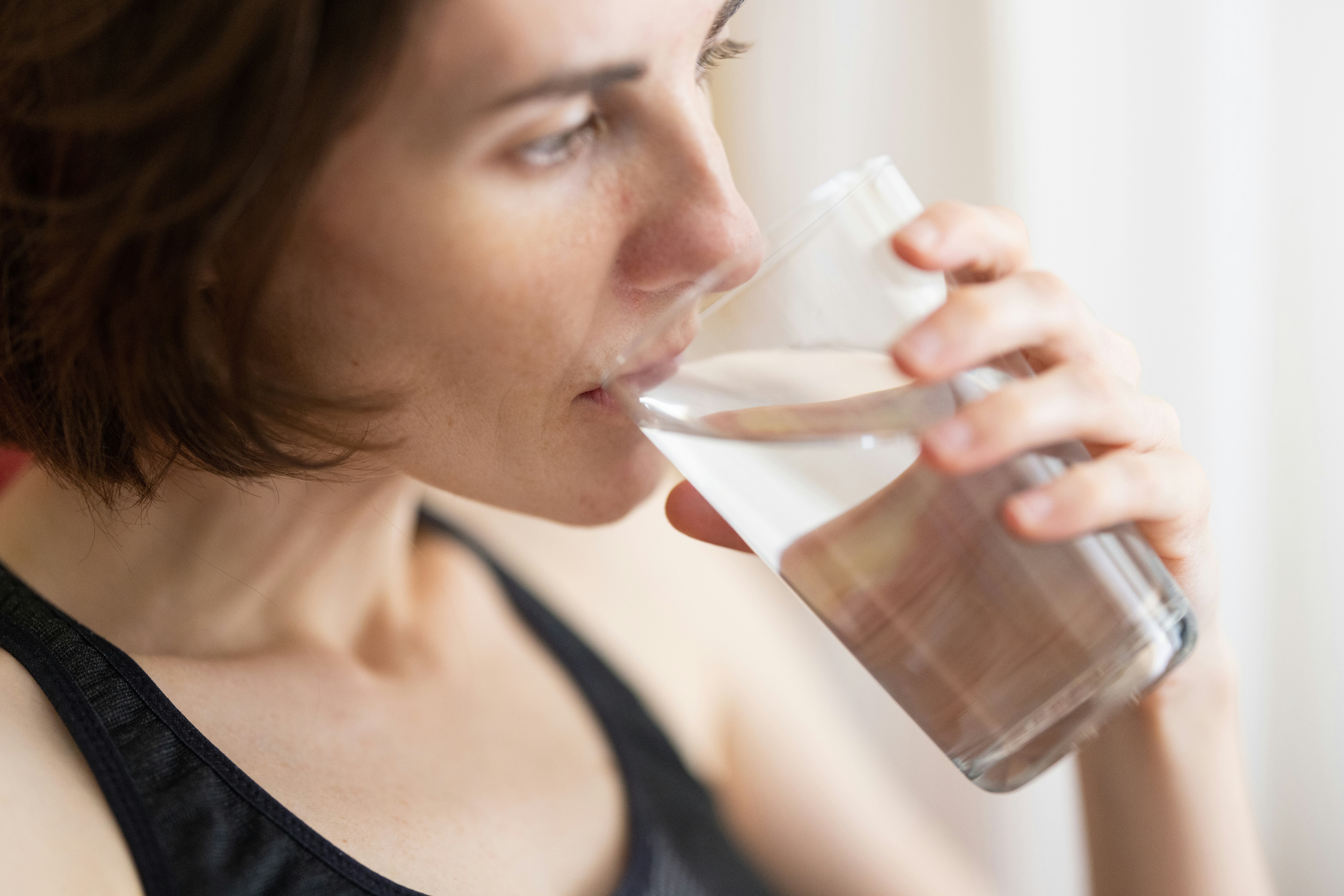 Woman in black tank top drinking water.